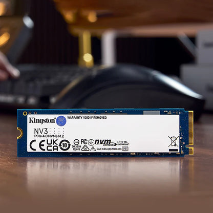 Kingston NVMe solid-state drive on a desk with a blurred computer setup in the background